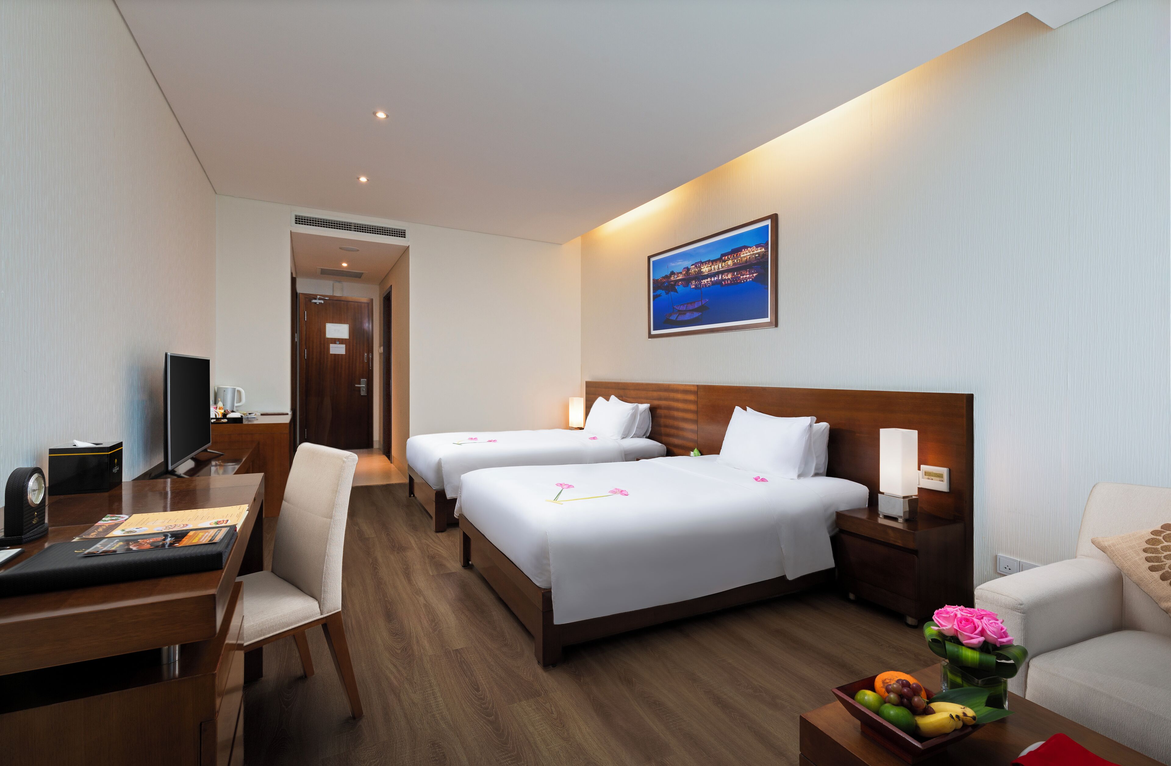 A hotel room with two beds, a desk, a chair, a TV, and a painting on the wall.