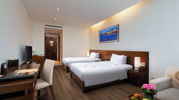 A hotel room with two beds, a desk, a chair, a TV, and a painting on the wall.