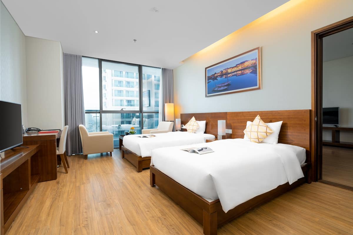 A hotel room with two beds, a desk, a chair, a TV, and a large window with a city view.