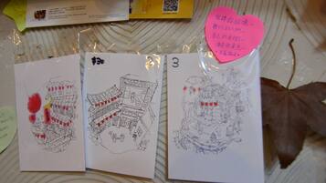 Three hand-drawn sketches of buildings on a table with a QR code, a heart-shaped note, and a brown leaf.