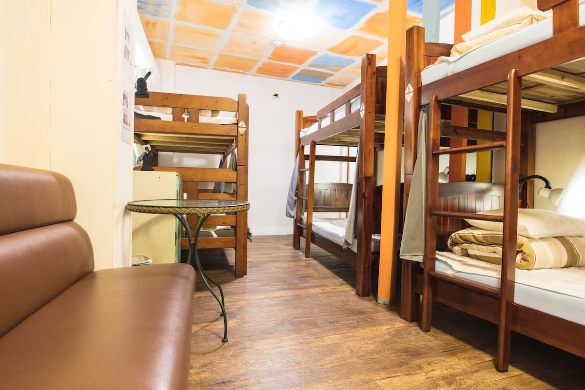 A bunk bed room with a wooden floor, a small table, and a leather couch.