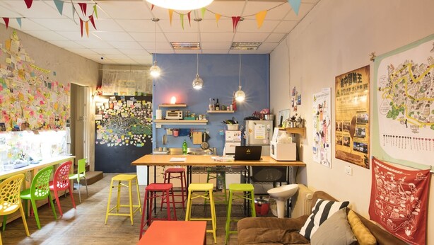Ein gemütliches Zimmer mit Küchenzeile, bunten Stühlen, einem braunen Sofa und einer Karte an der Wand.