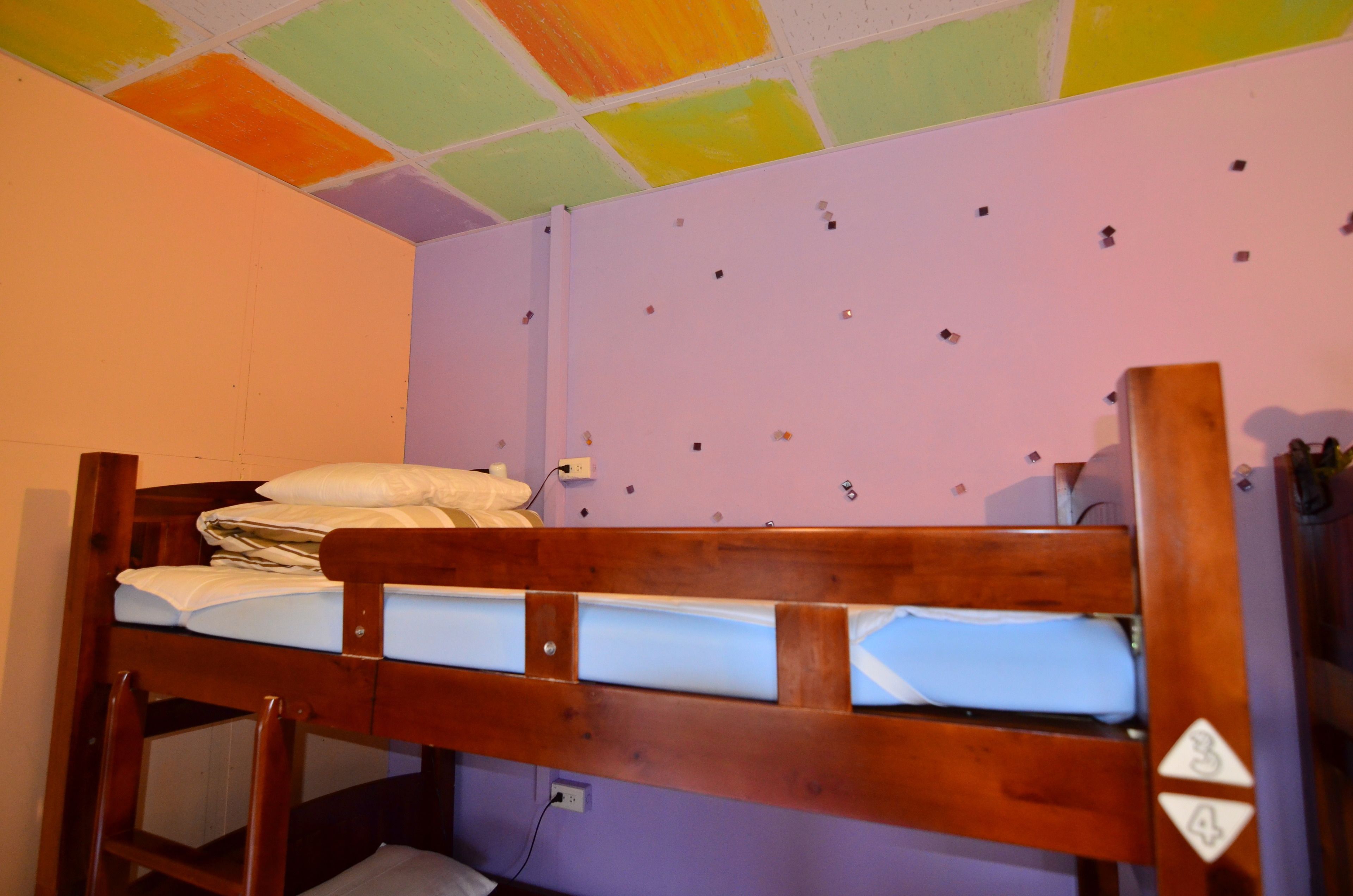A bunk bed in a room with a purple wall and a ceiling with multicolored tiles.