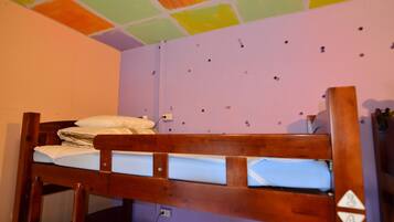 A bunk bed in a room with a purple wall and a ceiling with multicolored tiles.