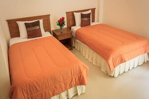 Two single beds with wooden headboards, a nightstand with a vase of flowers, and a plain wall.