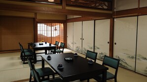 Ein traditioneller japanischer Raum mit Tatami-Boden, einem niedrigen Tisch mit Stühlen und Schiebetüren mit Landschaftsbild.