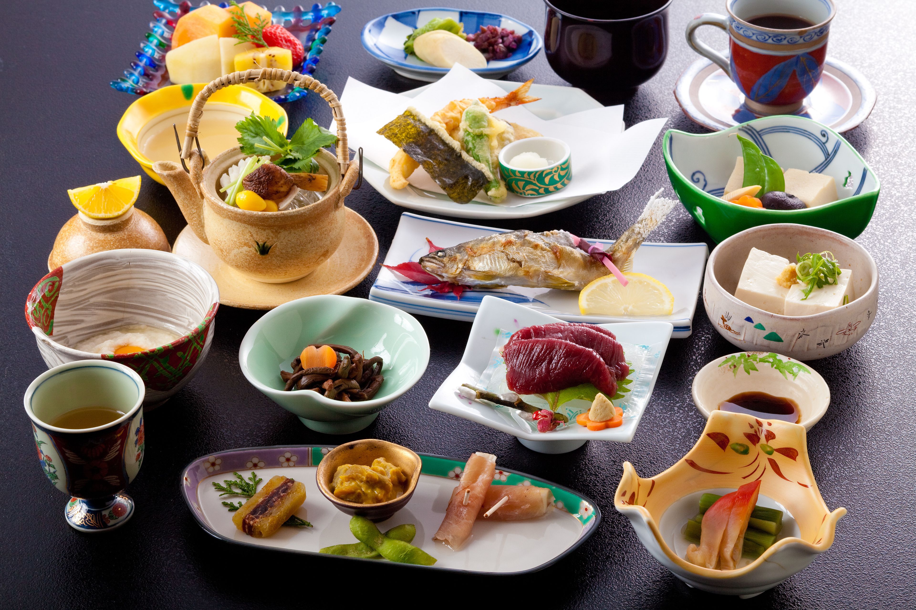 A variety of dishes and beverages on a table, including sushi, sashimi, and a bowl of soup.