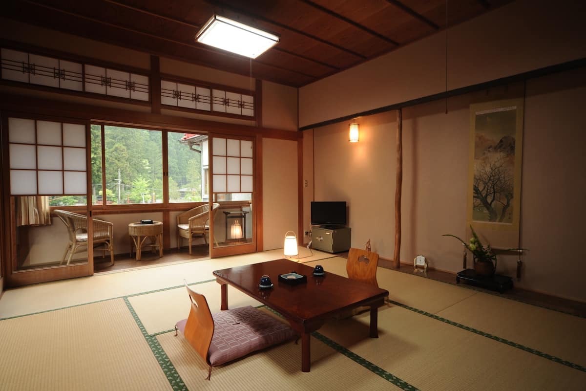 Une pièce de style japonais traditionnel, avec un sol recouvert de tatamis, une petite table en bois, un téléviseur et une porte coulissante donnant sur un balcon.