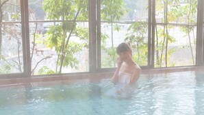 Eine Person in einem Schwimmbecken mit Blick auf Bäume und Gebäude durch große Fenster.