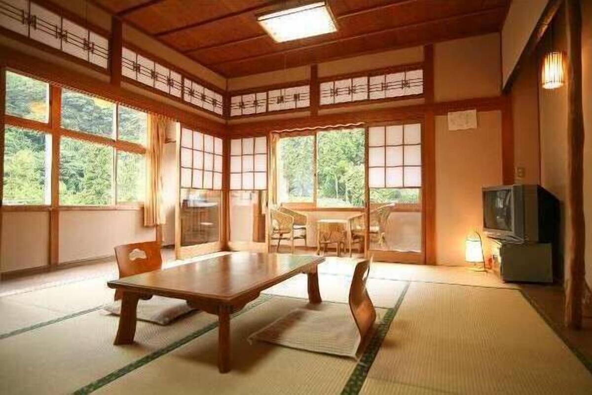 Une pièce de style japonais traditionnel, avec un sol recouvert de tatamis, une table basse, des chaises et un téléviseur.