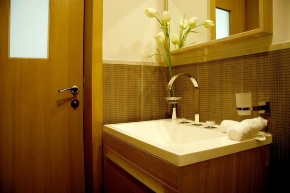 A bathroom with a wooden door, a white sink, a mirror, and a vase with white flowers.