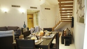 A modern dining area with a wooden staircase, a sofa, and a dining table set for a meal. -  Sealoft Villas (Amwaj Islands)