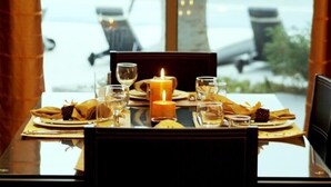 A dining table set for two with a candle, glasses, and plates, overlooking a view of chairs and a building. -  Sealoft Villas (Amwaj Islands)