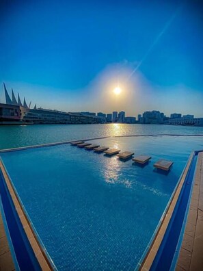 A swimming pool with a view of a city skyline and the sun setting over the water.