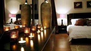 A hotel room with a large mirror reflecting a bed, bedside lamps, and a row of lit candles on a table. -  Sealoft Villas (Amwaj Islands)