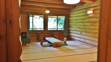 A wooden cabin interior with a tatami mat floor, a wooden dining table, and chairs.