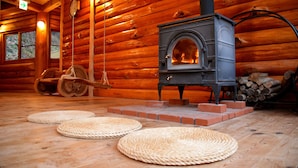 L’intérieur d’une cabane en rondins, avec un poêle à bois, des tapis tissés sur le sol et une horloge au mur.