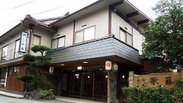 A traditional Japanese building with a tiled roof, a wooden entrance, and a signboard.