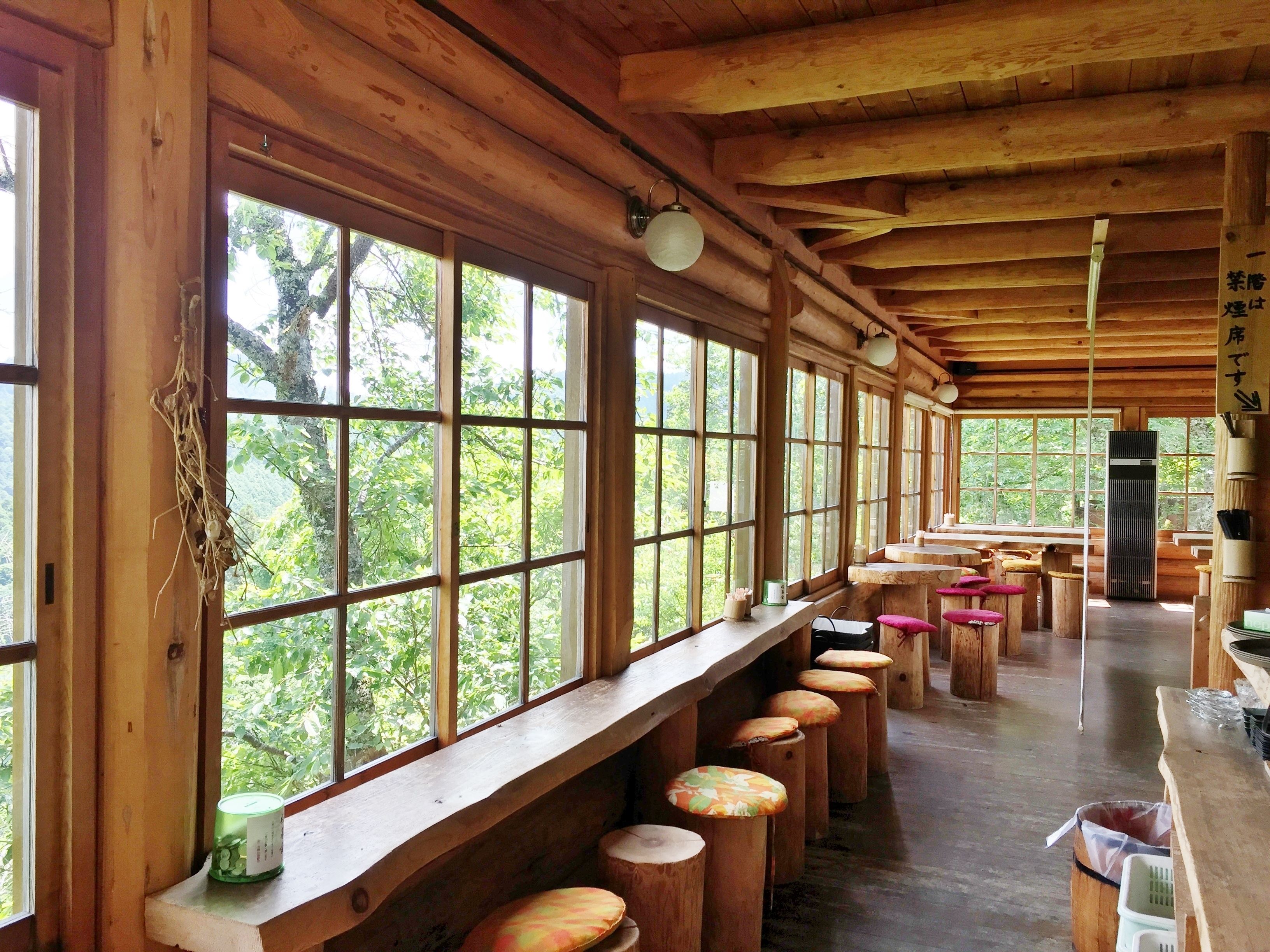 A wooden interior with large windows, wooden stools, and a long counter.