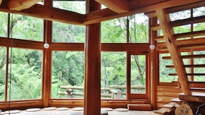 Une cabane en bois dotée de grandes fenêtres, d’une terrasse en bois et offrant une vue sur la forêt.