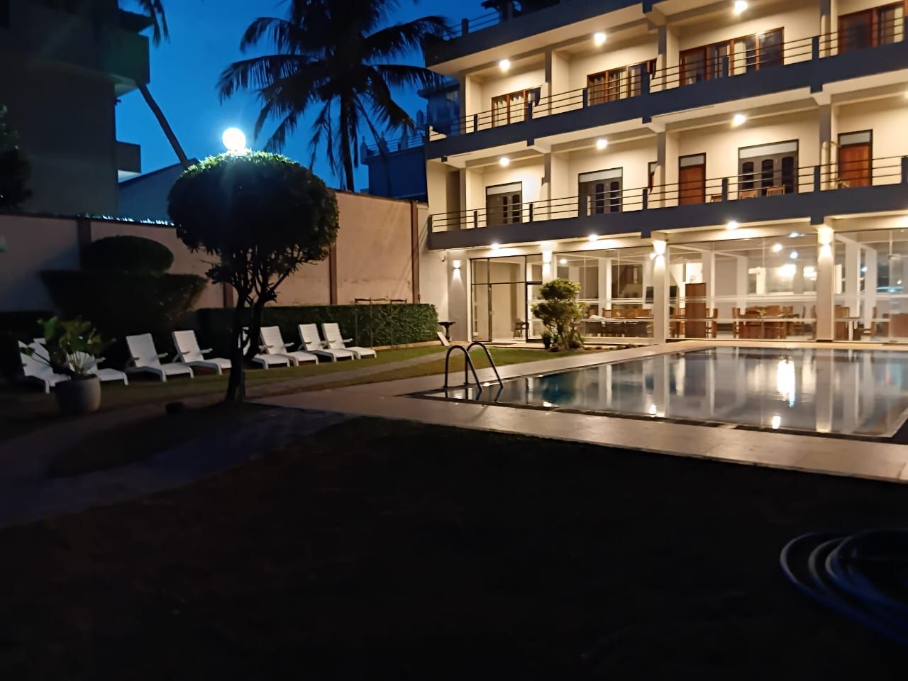 A hotel with a swimming pool, lounge chairs, and a well-lit building facade.