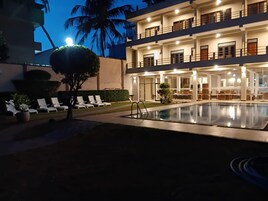 Un hotel con piscina, sillones de descanso y una fachada iluminada.