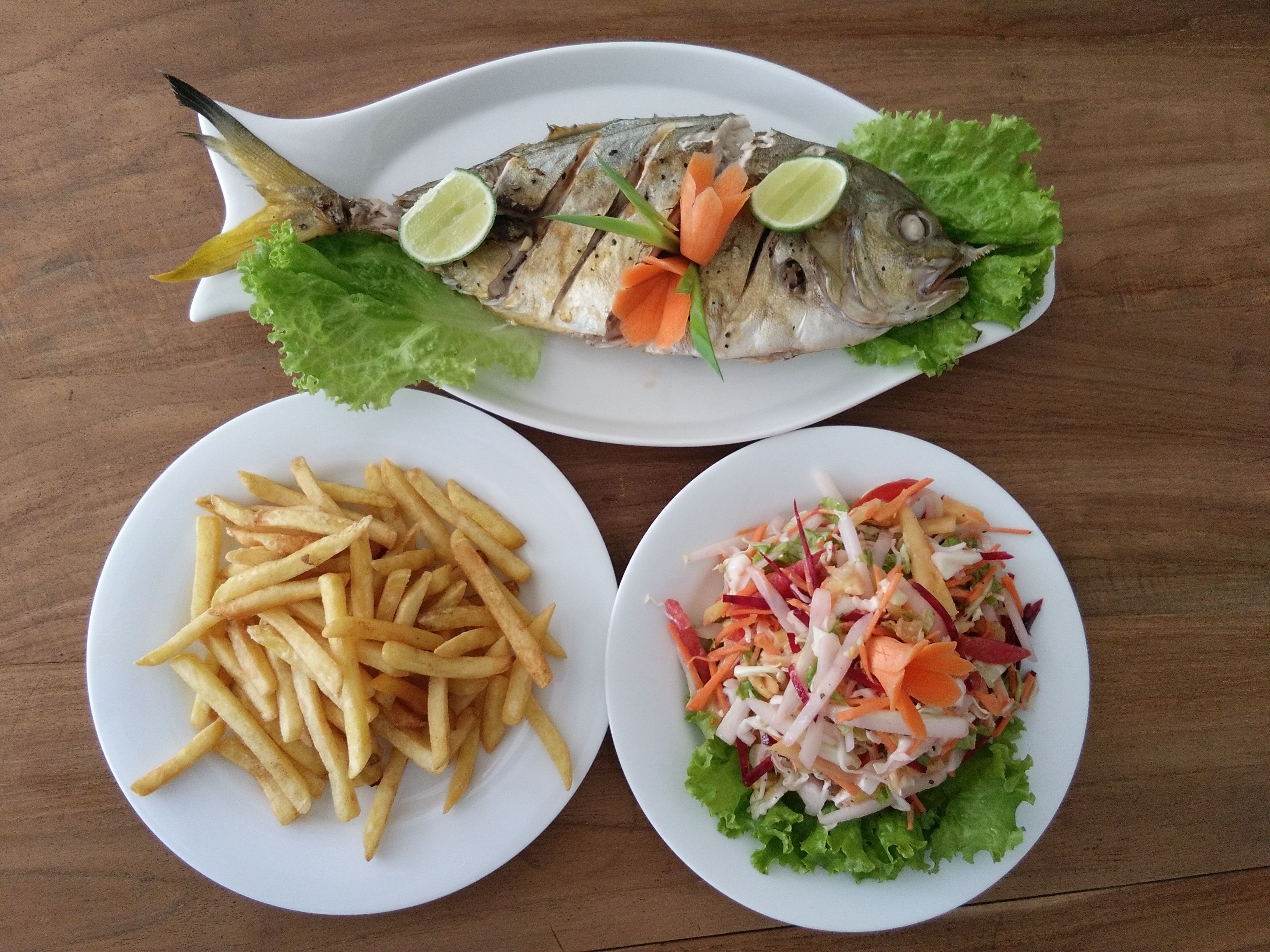A plate with grilled fish, French fries, and a vegetable salad.