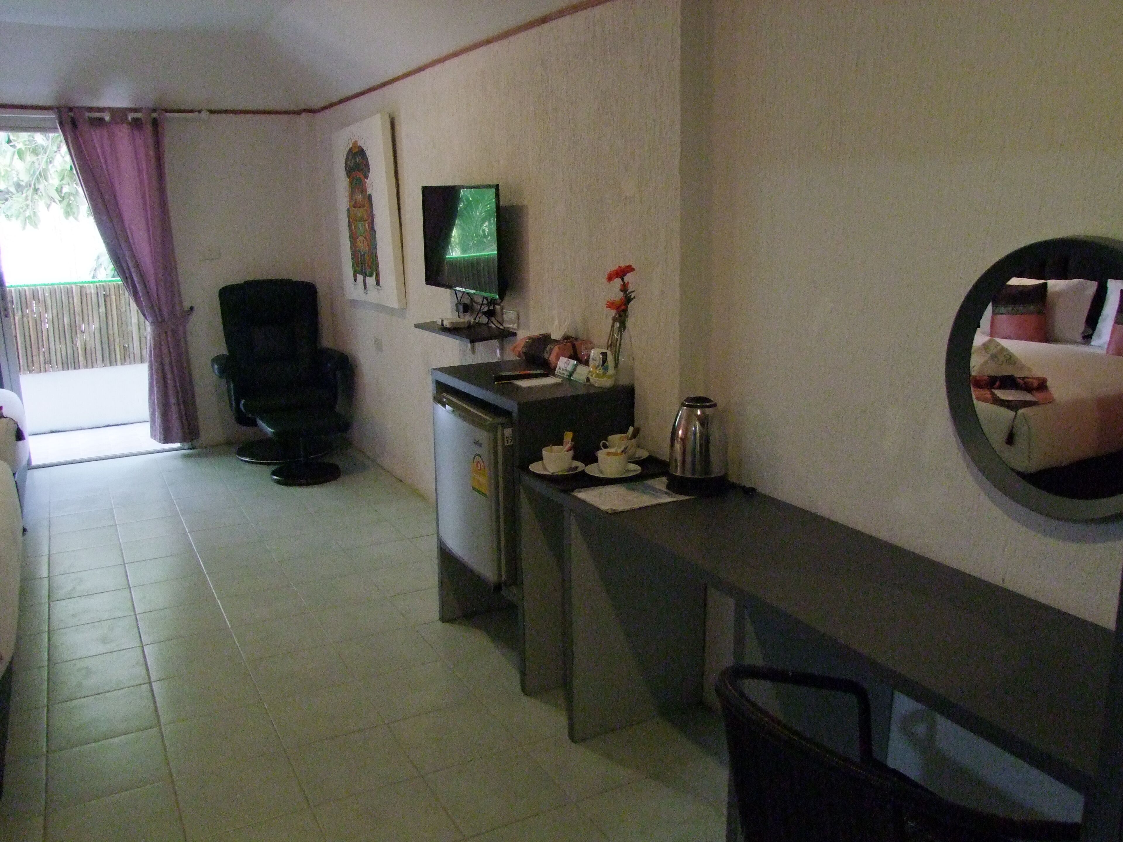A room with a desk, a chair, a television, a coffee maker, and a mirror on the wall.