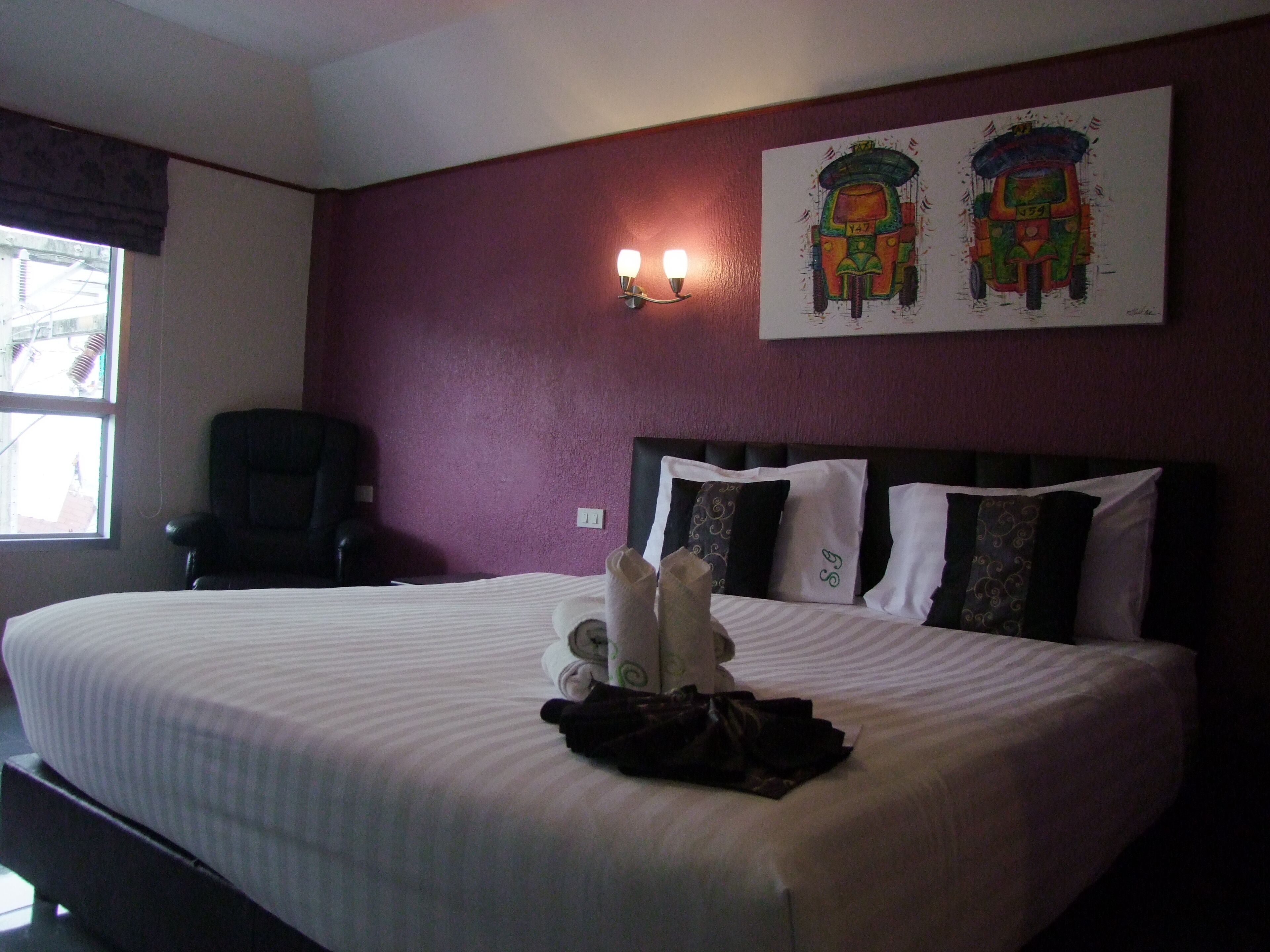 A hotel room with a large bed, a chair, and two wall-mounted lamps.
