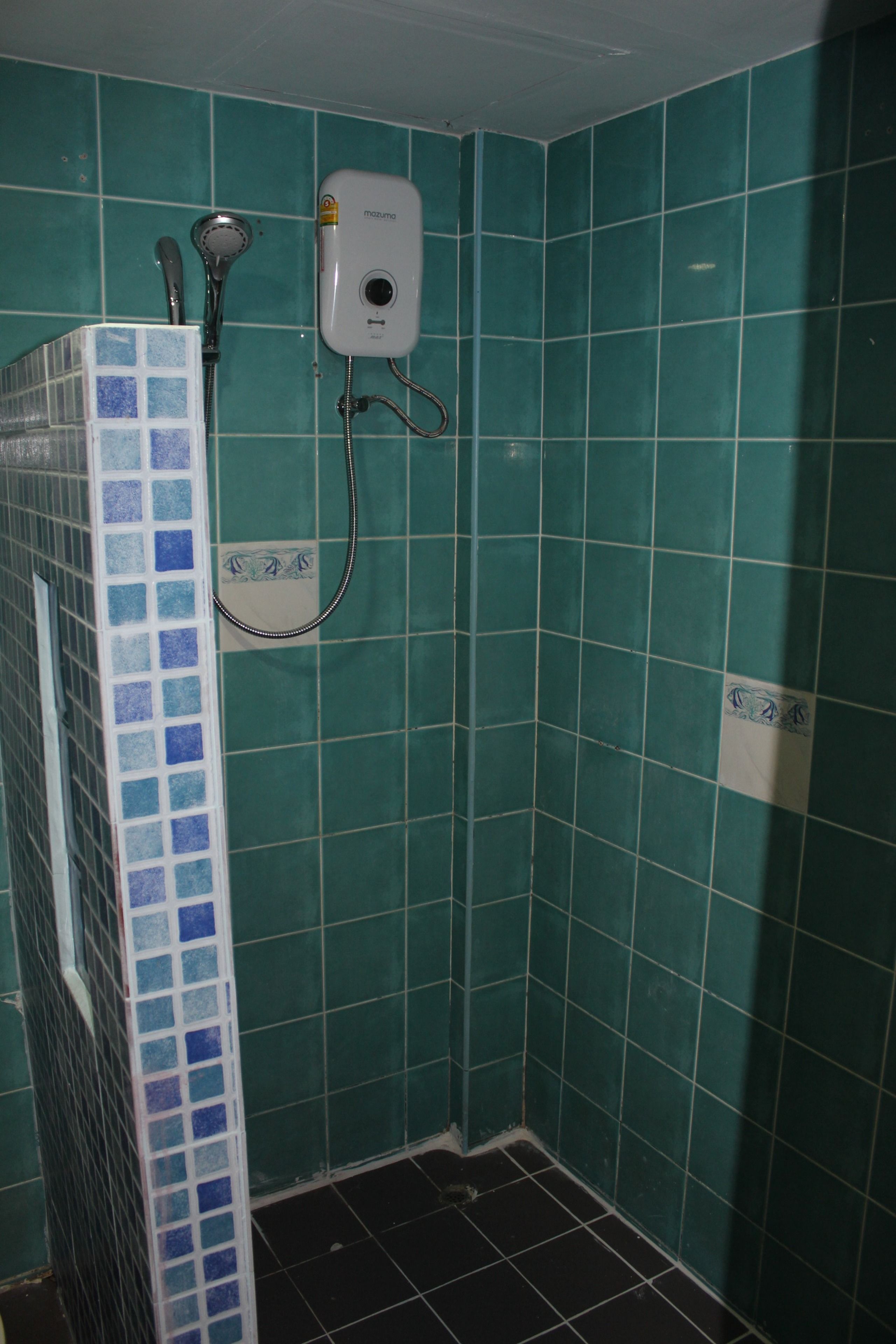 Un baño pequeño con azulejos verde azulado, una ducha y un inodoro.