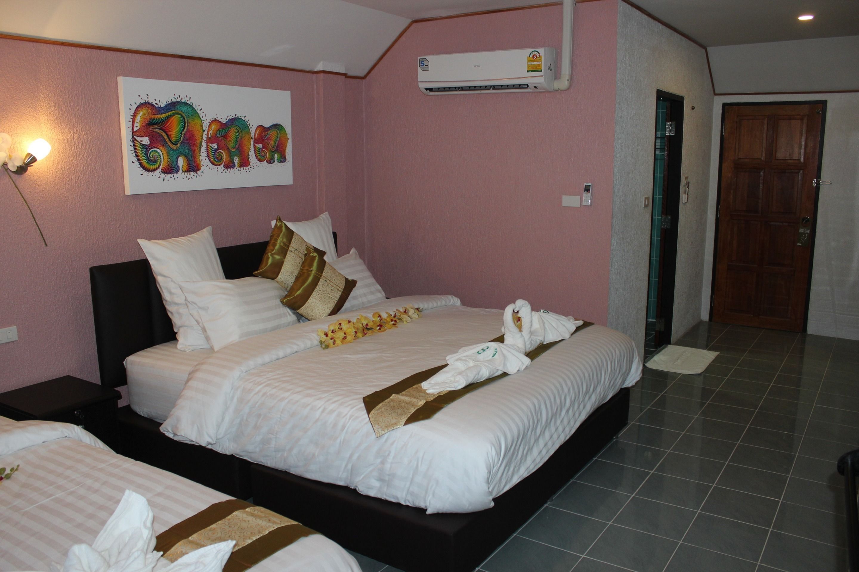 A hotel room with a large bed, two smaller beds, a wall-mounted air conditioner, and a wooden door.