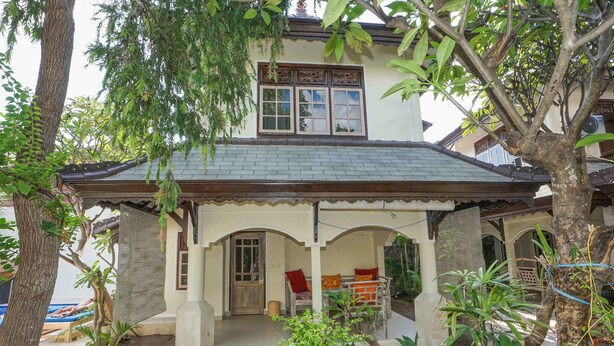 A two-story house with a covered porch, a window with decorative shutters, and a small garden area with potted plants. - Martas Hotel Gili Trawangan (Gili Trawangan)
