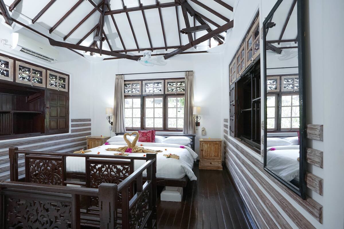 A traditional room with a wooden ceiling, a bed with white linens, a wooden cabinet, and a large mirror.