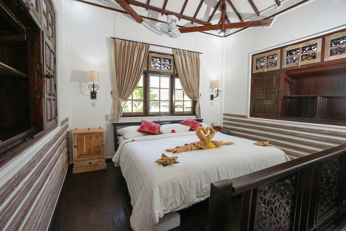A bedroom with a bed, a window with curtains, a nightstand, and a wall-mounted lamp.
