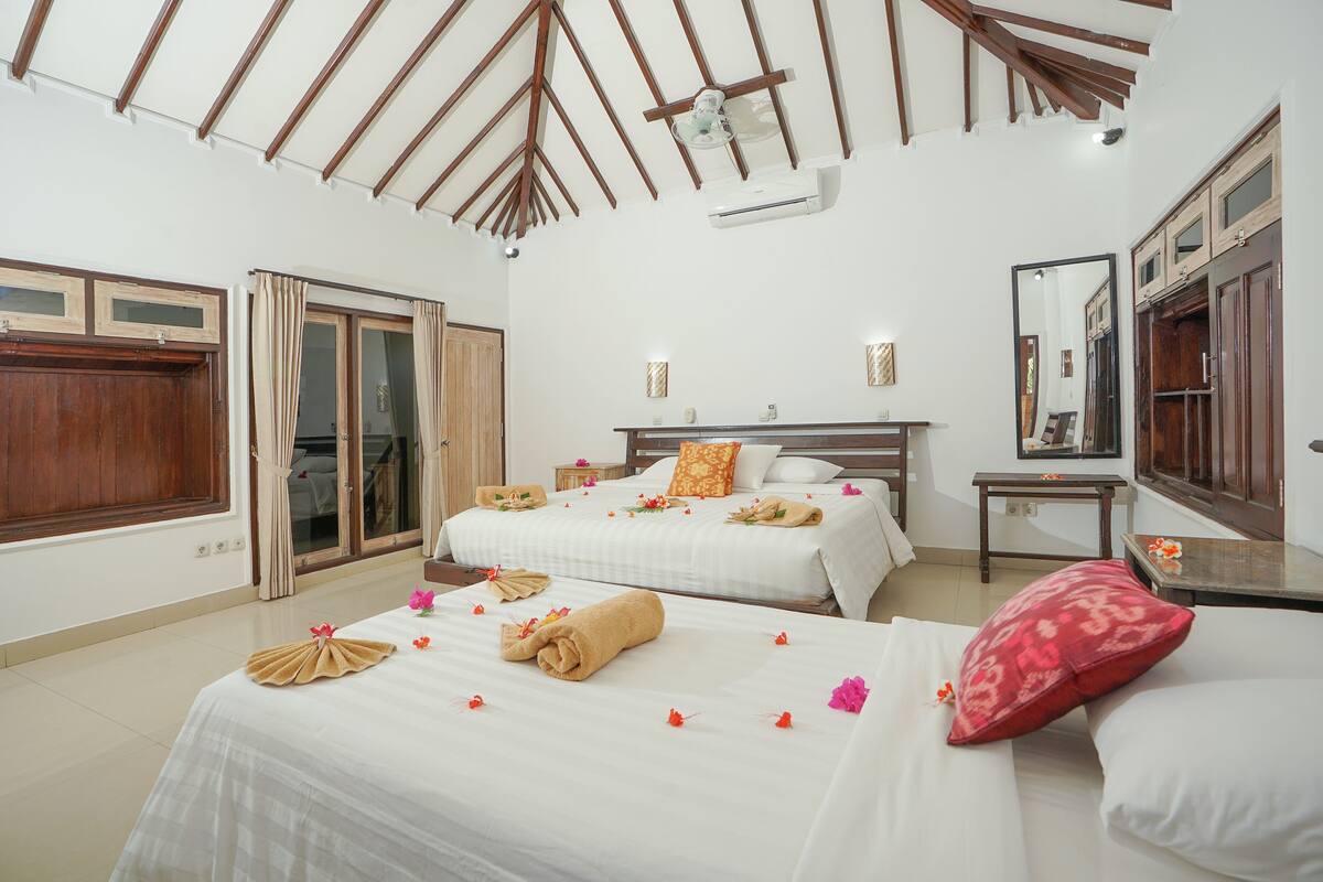 A hotel room with two beds, a wooden ceiling, a large mirror, and a sliding door.