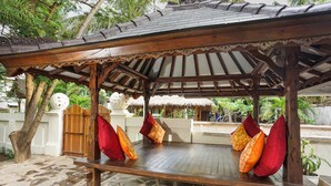 A wooden bench with cushions under a thatched roof structure. - Martas Hotel Gili Trawangan (Gili Trawangan)