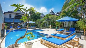 A pool area with lounge chairs and umbrellas, surrounded by potted plants and traditional architecture. - Martas Hotel Gili Trawangan (Gili Trawangan)