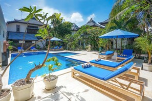A pool area with lounge chairs and umbrellas, surrounded by potted plants and traditional architecture. - Martas Hotel Gili Trawangan (Gili Trawangan)