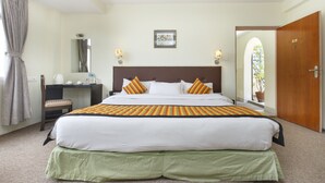 Una habitación de hotel con una cama grande, un escritorio, una silla, un espejo y una puerta.