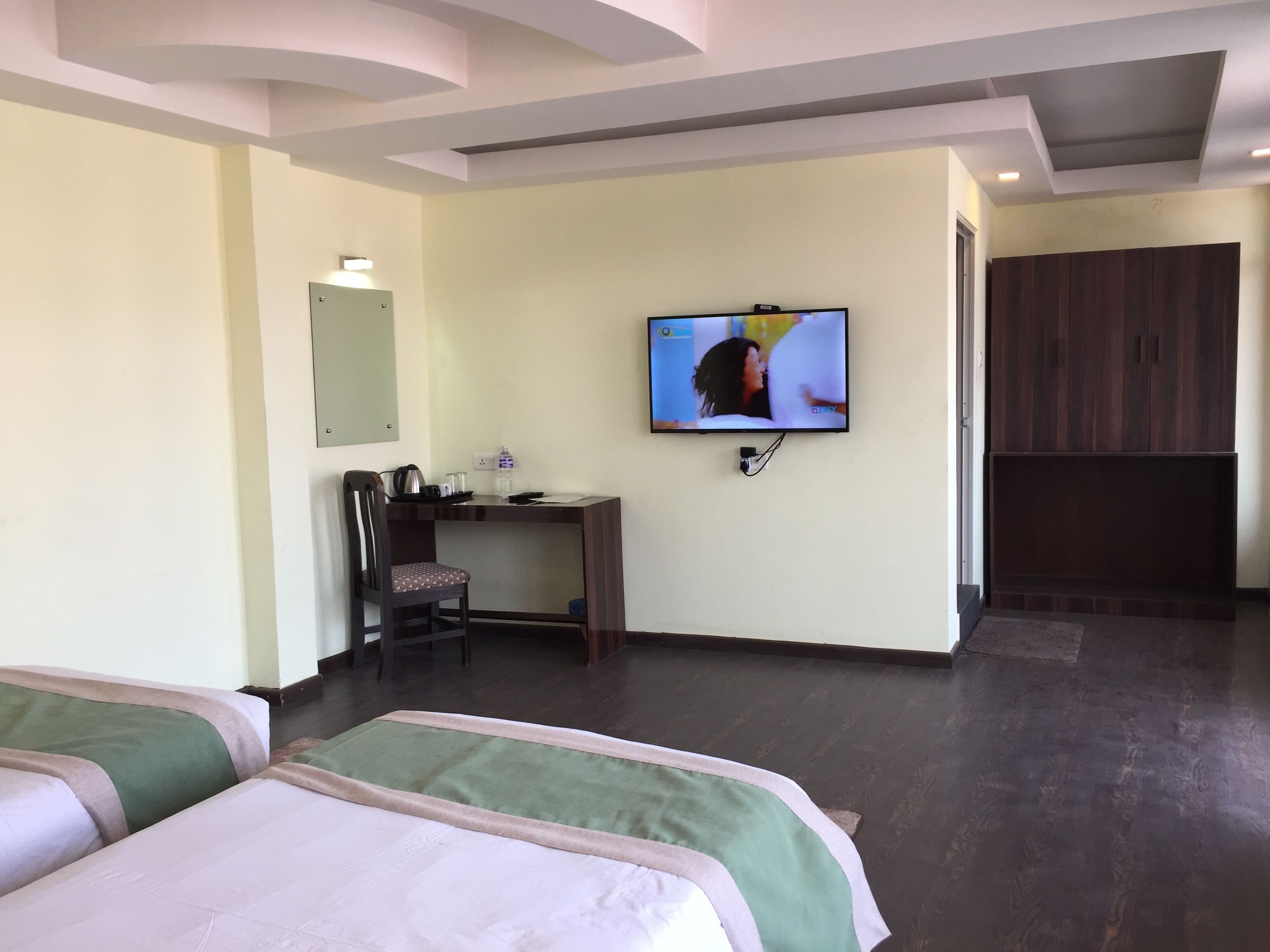 A hotel room with two beds, a desk with a chair, a television on the wall, and a wardrobe.