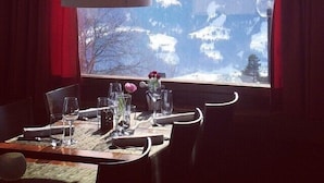 Un comedor con una mesa preparada para dos, una lámpara colgante y una ventana con vista a las montañas.