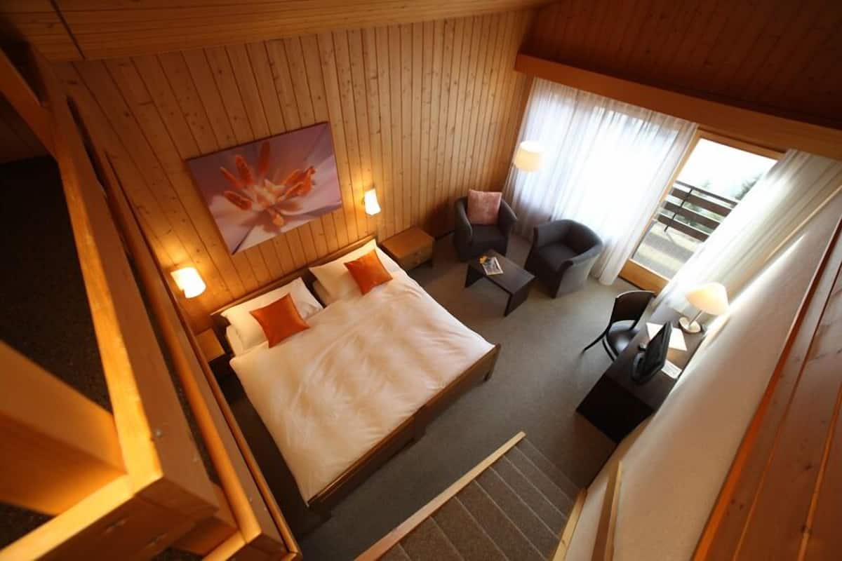 A room with a bed, two chairs, a small table, and a painting on the wall.