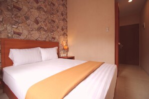 Una cama bien tendida con sábanas blancas y un plaid marrón, un cabecero de madera y una pared de piedra al fondo.