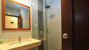 A bathroom with a wooden door, a glass shower enclosure, and a sink with a mirror above it. - Amaya Suites (Pogung Lor)
