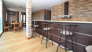 A modern kitchen with a stone backsplash, wooden bar stools, and a flat-screen TV mounted on the wall. - Amaya Suites (Pogung Lor)