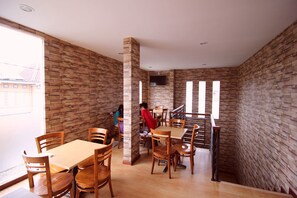 Un comedor con mesas y sillas de madera, paredes de piedra y una escalera.