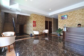 A hotel lobby with a reception desk, seating area, and a staircase.
