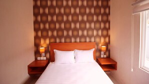 A hotel room with a large bed, wooden headboard, two bedside tables with lamps, and a patterned wall. - Amaya Suites (Pogung Lor)