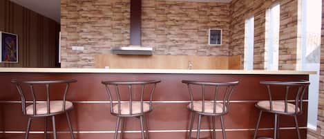 A kitchen with a stone backsplash, a central range hood, and three bar stools with cushioned seats.