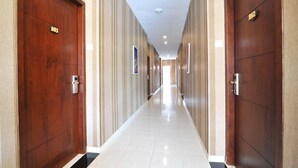 A hotel hallway with wooden doors, numbered room signs, and a tiled floor. - Amaya Suites (Pogung Lor)